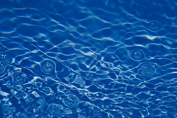 Defocus模糊了透明的蓝色清晰平静的水面纹理与水花和气泡 潮流抽象的自然背景 阳光下的水波有复制空间 蓝色水彩斑斓 — 图库照片