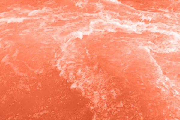 Defocus blurred transparent orange colored clear calm water surface texture with splash, bubble. Shining orange water ripple background. Surface of water in swimming pool. Orange bubble water shine.