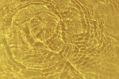 Defocus blurred transparent gold colored clear calm water surface texture with splashes and bubbles. Trendy abstract nature background. Water waves in sunlight with caustics. Yellow water shinning