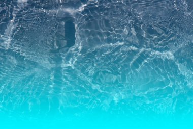 Yüzeyinde dalgalanmalar olan mavi su. Defocus bulanık mavi şeffaf, berrak, durgun su yüzeyi dokusu sıçrama ve kabarcıklarla bulanıklaştırılmış. Parlak desenli arka planda su dalgaları.