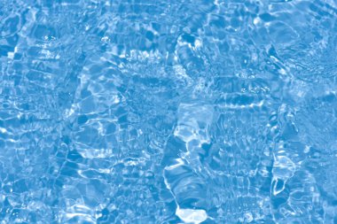 Yüzeyinde dalgalanmalar olan mavi su. Defocus bulanık mavi şeffaf, berrak, durgun su yüzeyi dokusu sıçrama ve kabarcıklarla bulanıklaştırılmış. Parlak desenli arka planda su dalgaları.