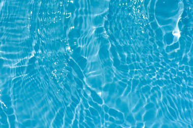 Yüzeyinde dalgalanmalar olan mavi su. Defocus bulanık mavi şeffaf, berrak, durgun su yüzeyi dokusu sıçrama ve kabarcıklarla bulanıklaştırılmış. Parlak desenli arka planda su dalgaları.