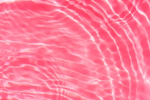 Red water background. Red water splashes on the surface ripple blur. Defocus blurred transparent pink colored clear calm water surface texture with splash and bubble. Red water waves shine.