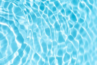 Yüzeydeki mavi su dalgaları bulanıklaştı. Defocus bulanık mavi şeffaf, berrak, durgun su yüzeyi dokusu sıçrama ve kabarcıklarla bulanıklaştırılmış. Parlak desenli arka planda su dalgaları.