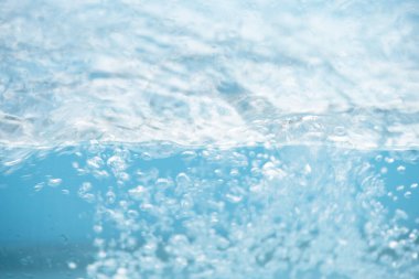 Yüzeydeki mavi su dalgaları bulanıklaştı. Defocus bulanık mavi şeffaf, berrak, durgun su yüzeyi dokusu sıçrama ve kabarcıklarla bulanıklaştırılmış. Parlak desenli arka planda su dalgaları.