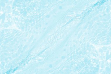 Yüzeydeki mavi su dalgaları bulanıklaştı. Defocus bulanık mavi şeffaf, berrak, durgun su yüzeyi dokusu sıçrama ve kabarcıklarla bulanıklaştırılmış. Parlak desenli arka planda su dalgaları.