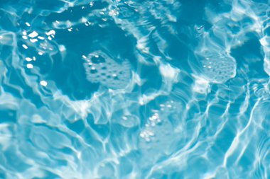 Yüzeyinde dalgalanmalar olan mavi su. Defocus bulanık mavi şeffaf, berrak, durgun su yüzeyi dokusu sıçrama ve kabarcıklarla bulanıklaştırılmış. Parlak desenli arka planda su dalgaları.