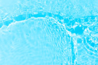 Yüzeydeki mavi su dalgaları bulanıklaştı. Defocus bulanık mavi şeffaf, berrak, durgun su yüzeyi dokusu sıçrama ve kabarcıklarla bulanıklaştırılmış. Parlak desenli arka planda su dalgaları.