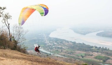 Gökyüzünde paraşütle atlıyor. Paraglider, Tayland 'ın Nongkhai kentindeki Wat Pha Tak Suea' daki Güzel Görüş Mekong Nehri 'nden manzara üzerinde uçuyor. Ekstrem spor kavramı, macera / meydan okuma.