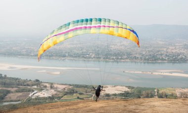 Gökyüzünde paraşütle atlıyor. Paraglider, Tayland 'ın Nongkhai kentindeki Wat Pha Tak Suea' daki Güzel Görüş Mekong Nehri 'nden manzara üzerinde uçuyor. Ekstrem spor kavramı, macera / meydan okuma.