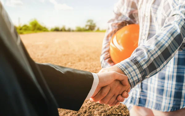 Business handshake land purchase. Businessman handshake a deal with a realtor for the construction of a house project. Empty reclamation soil in real estate sale or property investment concept.