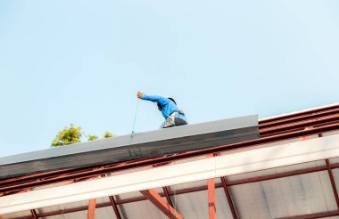 Özel koruma işinde çalışan çatıcı eldiven giyer, hava veya pnömatik çivi tabancası kullanır, yeni çatının tepesine asfalt kiremit yerleştirir, inşaat halindeki konut kavramı.