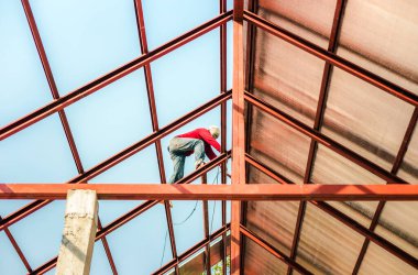 Özel koruma işinde çalışan çatıcı eldiven giyer, hava veya pnömatik çivi tabancası kullanır, yeni çatının tepesine asfalt kiremit yerleştirir, inşaat halindeki konut kavramı.