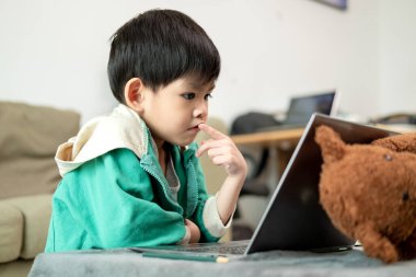 Asyalı çocuk çevrimiçi çalışıyor ve laptopta faaliyet gösteriyor.