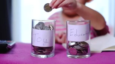 Asyalı erkek, elinde gümüş para var. Oyuncaklar ve eğitim arasında para biriktirmeyi seç..