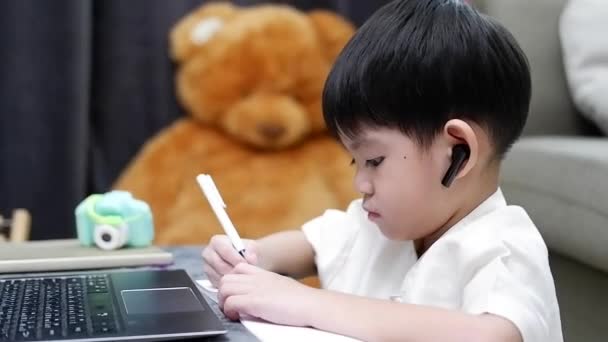Asiatischer Junge Hört Audio Und Schreibt Hausaufgaben Auf Während Online — Stockvideo