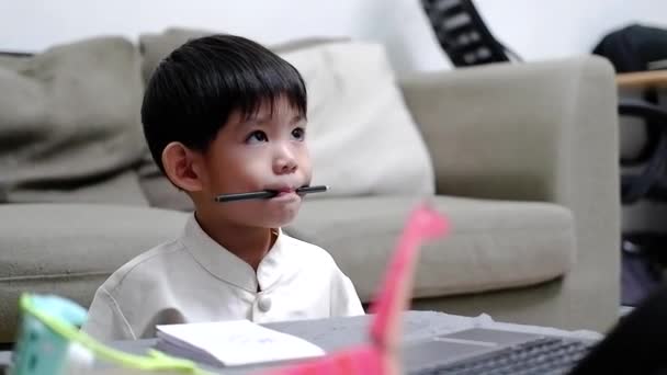 アジアの少年は口に鉛筆を保持し ノートパソコンでオンラインで勉強しながら退屈な表現を示しています — ストック動画