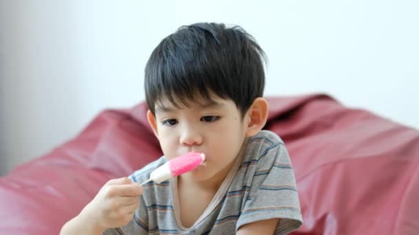 一个亚洲男孩正坐在椅子上吃着美味的冰淇淋 — 图库视频影像