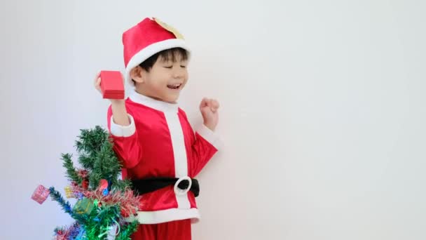 アジアの少年はサンタの衣装を着て 楽しいクリスマスツリーの近くで遊んでいます 4K解像度について — ストック動画
