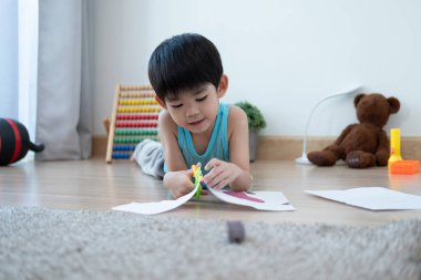 Asyalı çocuk makas kullanarak çizgi boyunca kağıt kesiyor. Sınıf dışından öğreniyor.