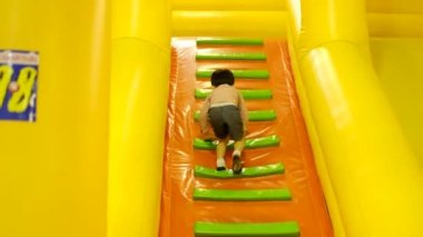 Küçük Asyalı çocuk şişme çocuk parkında merdivenleri tırmanıyor.