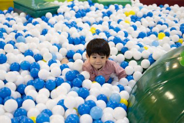 Küçük bir Asyalı çocuk topların arasında saklambaç oynuyordu.