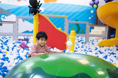 Küçük Asyalı çocuk yüzen bir topa bakıyor. Küçük topların arasında.