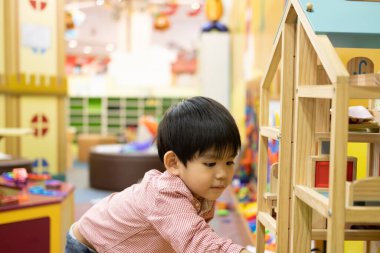 Küçük Asyalı çocuk oyuncak ahşap bir evin içinde oynuyor..