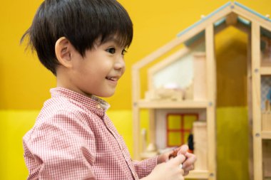 Küçük Asyalı çocuk oyuncak ahşap bir evin içinde oynuyor..