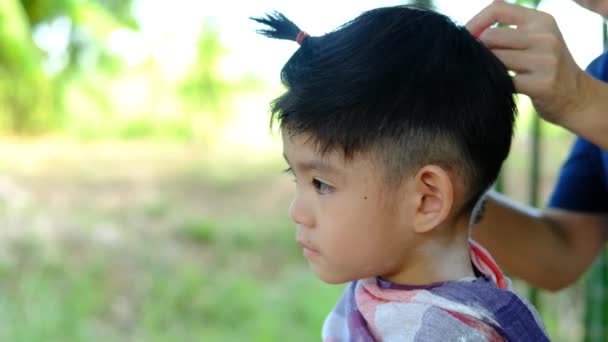 Holič Stříhá Vlasy Asijského Chlapce Otevřeném Prostoru Plném Stromů — Stock video