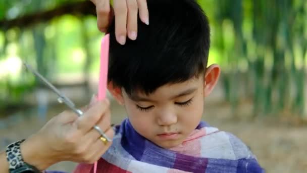 Holič Stříhá Vlasy Asijského Chlapce Otevřeném Prostoru Plném Stromů — Stock video