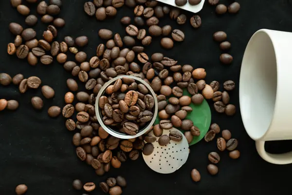Coffee beans inside and around a refillable coffee capsule on a black background.