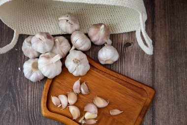 Büyük bir sarımsak kafası siyah bir arka planda, ahşap bir tabakta yatıyor..