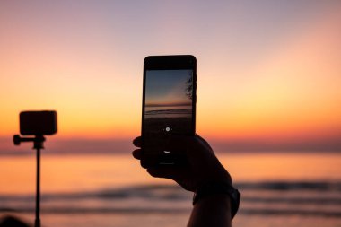 Turistin elleri gün batımında ve alacakaranlıkta denizin fotoğraflarını çekiyor..