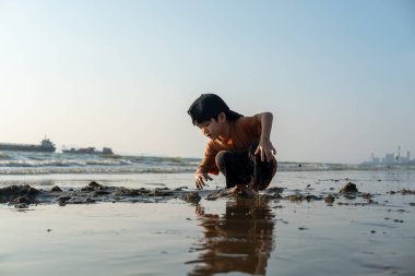 Küçük Asyalı çocuk kumsalda kumsalda oynuyor.