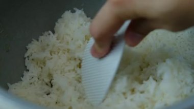 Bir adamın eli bir kepçeyle sıcak pirinç topluyor..