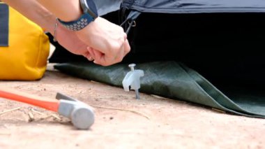 Tourists' hands use hammers to hammer into the ground to make the tents strong.