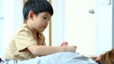 A young Asian child is taking care of his mother by massaging her muscles to relax her.