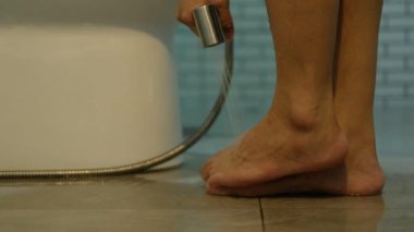 Bir kadının eli banyoda ayaklarını temizlemek için su püskürtücü kullanır..