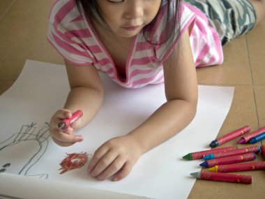 Asyalı bir kız mum boyayla resim yaparken yatar