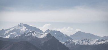 Dağ sırasının panoramik manzarası, karlı tepeler ve tepeler ve sıra dışı bulutlar, bulutlu gökyüzü ile tek renkli manzara