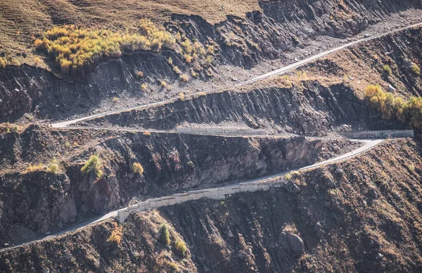 stock image A serpentine mountain road carved into the rock with several turns meanders among the mountains, a top view of the mountain route in autumn