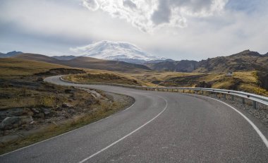 Sonbaharda dağlarda sarmal asfalt karayolu Elbrus Dağı 'nın arka planına karşı, Ekim ayında dağlarda güzel bir yol.