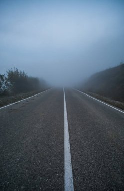 Dağlardaki otomobil yolu sonbaharın sonlarında bulutların ve sislerin içine iniyor, siste görüş mesafesi düşük bir hat.