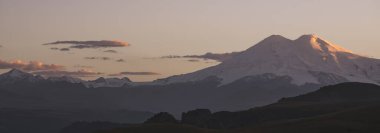 Gün batımında kar ve buzullarla kaplı Elbrus Dağı 'nın manzarası. Gün batımında aydınlatma, bulutlu gün batımı gökyüzü.