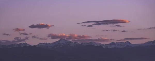 Panorama of a mountain range with peaks with snow and ice at sunset with a cloudy sky, mountain rocky peaks in autumn