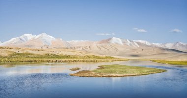 Yüksek dağ manzarası, dağlarda bir nehir bir dağ vadisinde yeşil çayırlar arasında dağların arka planına karşı akar, arka plan için Pamir Dağları 'ndaki manzara