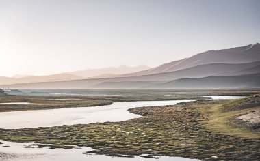 Yüksek dağ manzarası, dağlarda bir nehir bir dağ vadisinde yeşil çayırlar arasında dağların arka planına karşı akar, arka plan için Pamir Dağları 'ndaki manzara