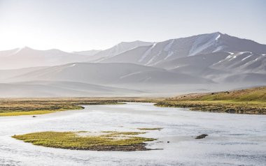 Yüksek dağ manzarası, dağlarda bir nehir bir dağ vadisinde yeşil çayırlar arasında dağların arka planına karşı akar, arka plan için Pamir Dağları 'ndaki manzara
