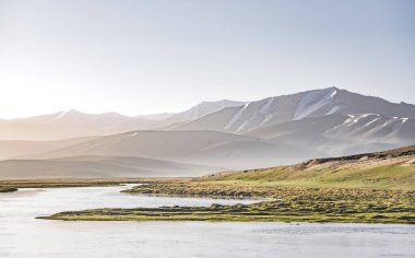 Yüksek dağ manzarası, dağlarda bir nehir bir dağ vadisinde yeşil çayırlar arasında dağların arka planına karşı akar, arka plan için Pamir Dağları 'ndaki manzara